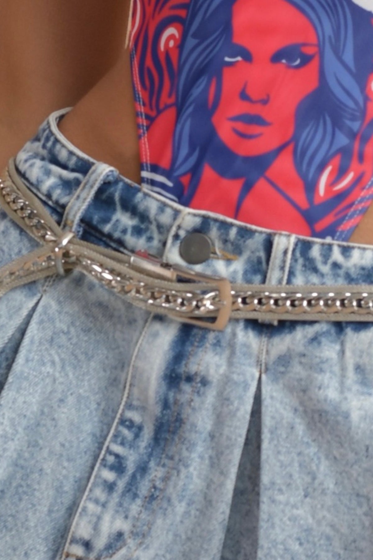 Close-up of a statement metal belt with chain details, styled with distressed denim and a vibrant concert-ready look.